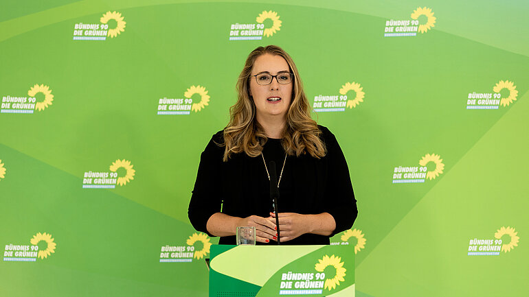 Katharina Dröge hinter einem Redepult vor einer Pressewand der grünen Bundestagsfraktion