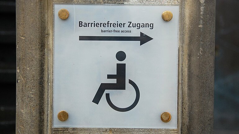 Schild mit Aufschrift barrierefrei, das ein Piktogramm einer Rollstuhlfahrerin zeigt