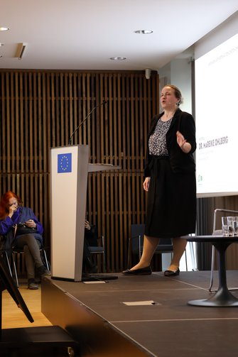 Eine Frau steht auf der Bühne und redet am Pult.