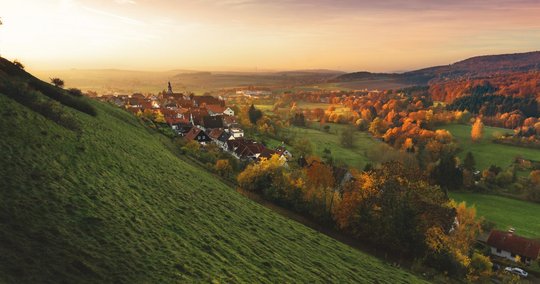 Eine Siedlung neben einem Berg, im Hintergrund geht die Sonne unter. 