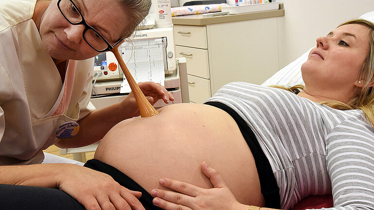 Hebamme horcht mit Hörrohr am Bauch einer schwangeren Frau