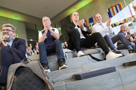 Menschen sitzen auf Treppenstufen in einem Saal