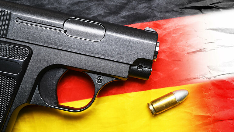 Waffe liegt auf Deutschlandfahne neben einer Patrone.
