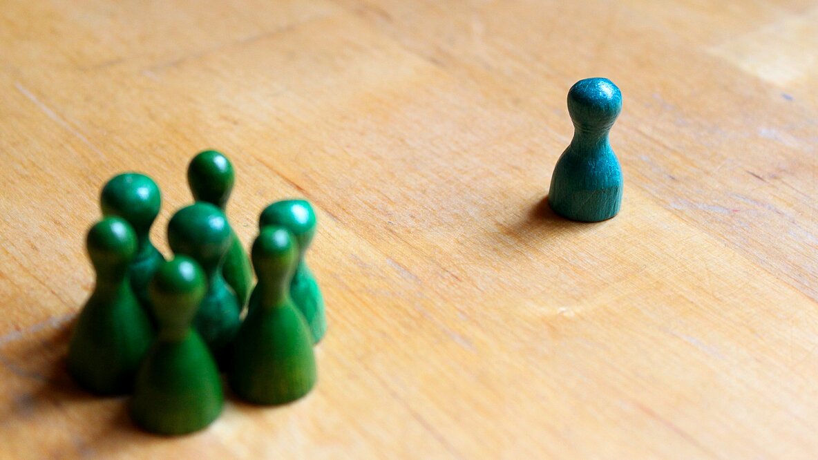 Mehrere grüne Spielfiguren in einer Gruppe, eine davon abseits stehend