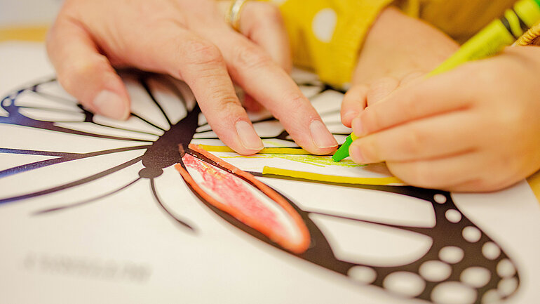 Kinderhand und Frauenhand malen Schmetterling mit Buntstiften