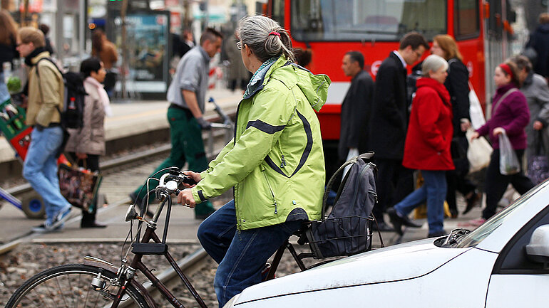 Fußgänger, Pkws und Radfahrer überqueren vor einer Straßenbahn in Köln eine Straße.