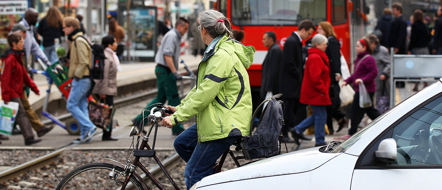 Fußgänger, Pkws und Radfahrer überqueren vor einer Straßenbahn in Köln eine Straße.