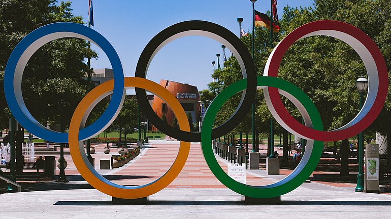 Olympische Ringe mit einer deutschen Fahne im Hintergrund