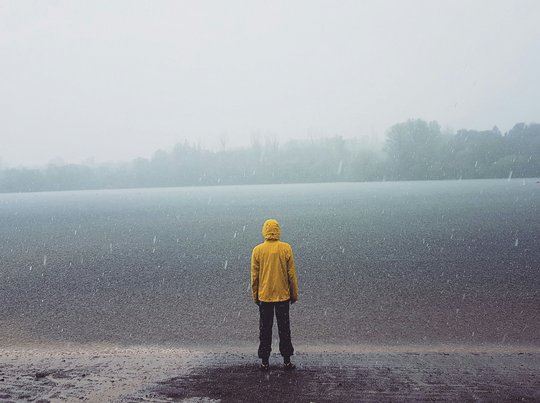 Eine Person mit einer gelben Regenjacke steht im Regen und blickt auf einen See