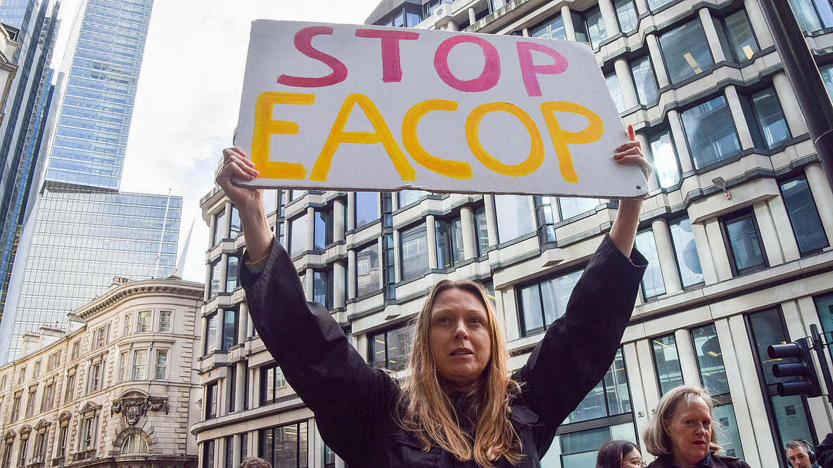 Eine Frau hält ein Schild hoch. Aufschrift: STOP EACOP