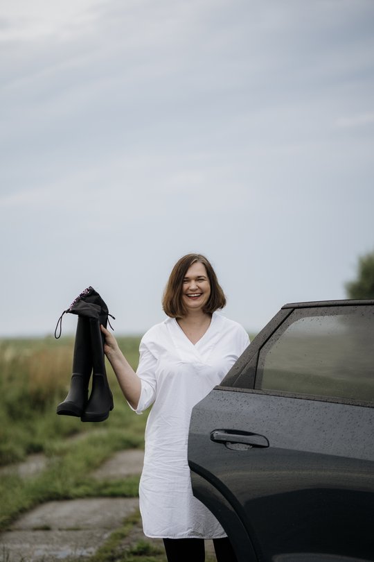 Die grüne Bundestagsabgeordnete Claudia Müller steht lachend mit Gummistiefeln in der Hand neben einem Auto, bereit für einen Ausflug ins Moor.