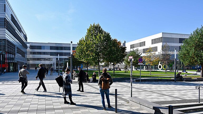 Studierende stehen und gehen auf einem Platz vor einem Universitätsgebäude 