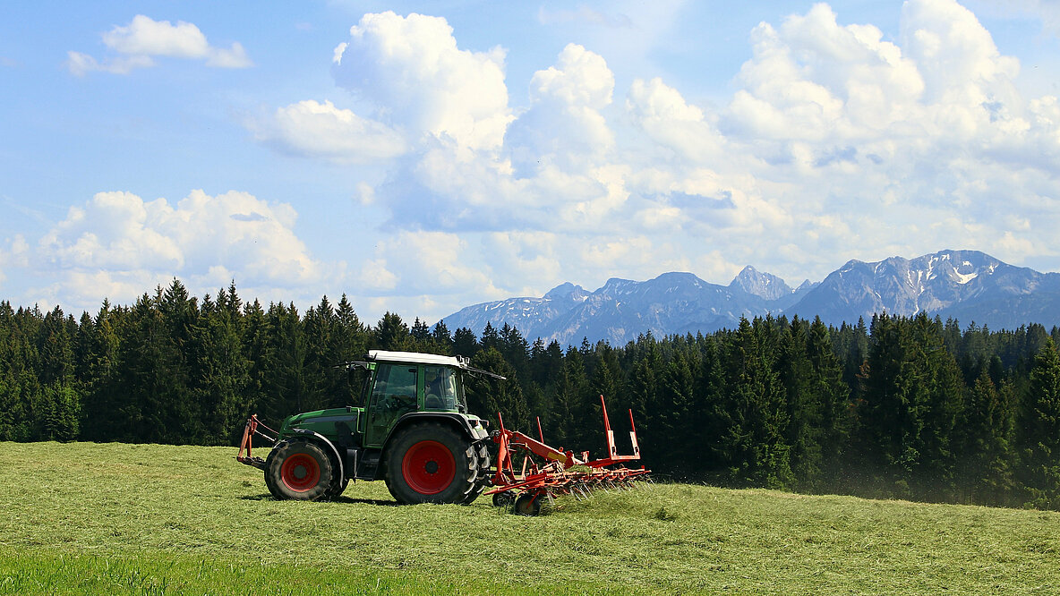Ein Traktor auf einem Feld vor den Alpen.