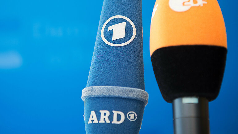 Mikrofone von ARD und ZDF vor blauem Hintergrund.