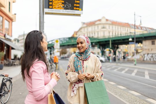 Zwei Frauen stehen in Berlin an einer Bushaltestelle. Eine Frau trägt ein Kopftuch.