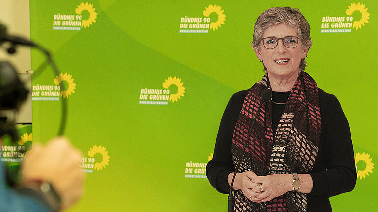 Die grüne Fraktionsvorsitzende Britta Haßelmann steht vor einer grünen Rückwand mit dem Sonnenblumen-Logo der Fraktion.