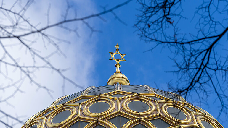 Die goldene Kuppel einer Synagoge mit Davidstern vor blauem Himmel.