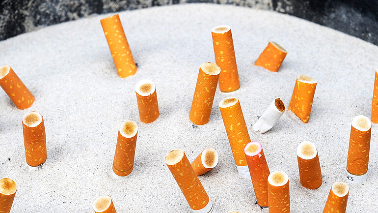 Zigarettenkippen stecken im Sand eines Aschenbechers.