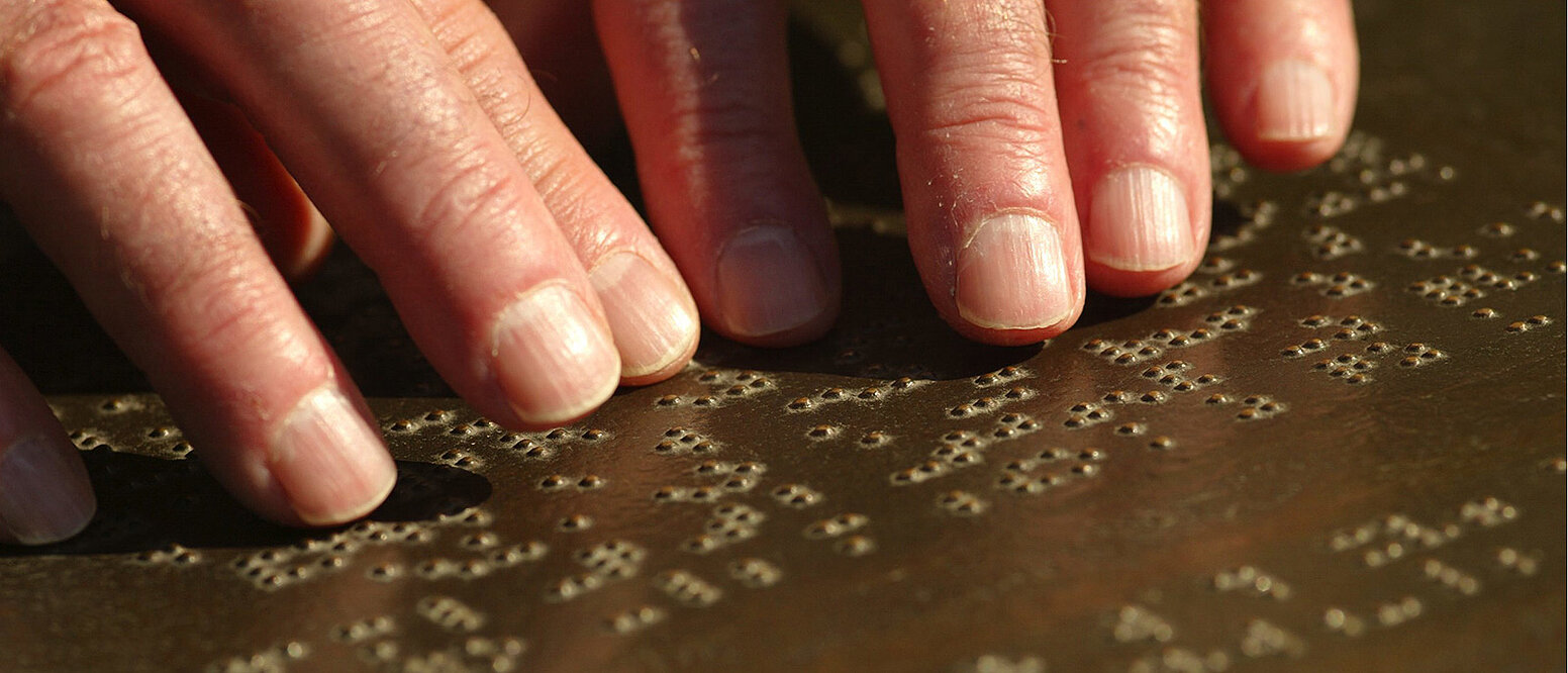 Sehbehinderter blinder Mann ertastet die Schriftzeichen (Blindenschrift) im japanischen Garten im Bonner Rheinauenpark. 