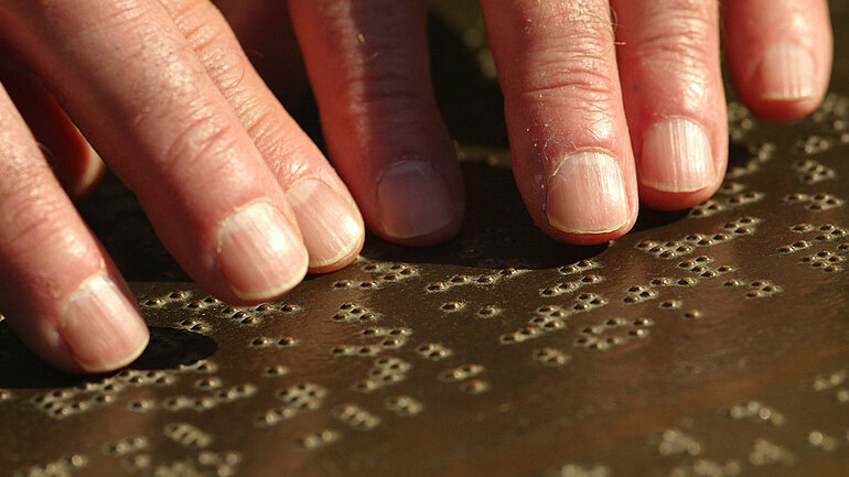 Sehbehinderter blinder Mann ertastet die Schriftzeichen (Blindenschrift) im japanischen Garten im Bonner Rheinauenpark. 