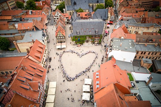 Hunderte Menschen in überwiegend hellen Shirts bilden auf dem Quedlinburger Marktplatz vor dem Rathaus ein großes Herz, aus der Vogelperspektive.