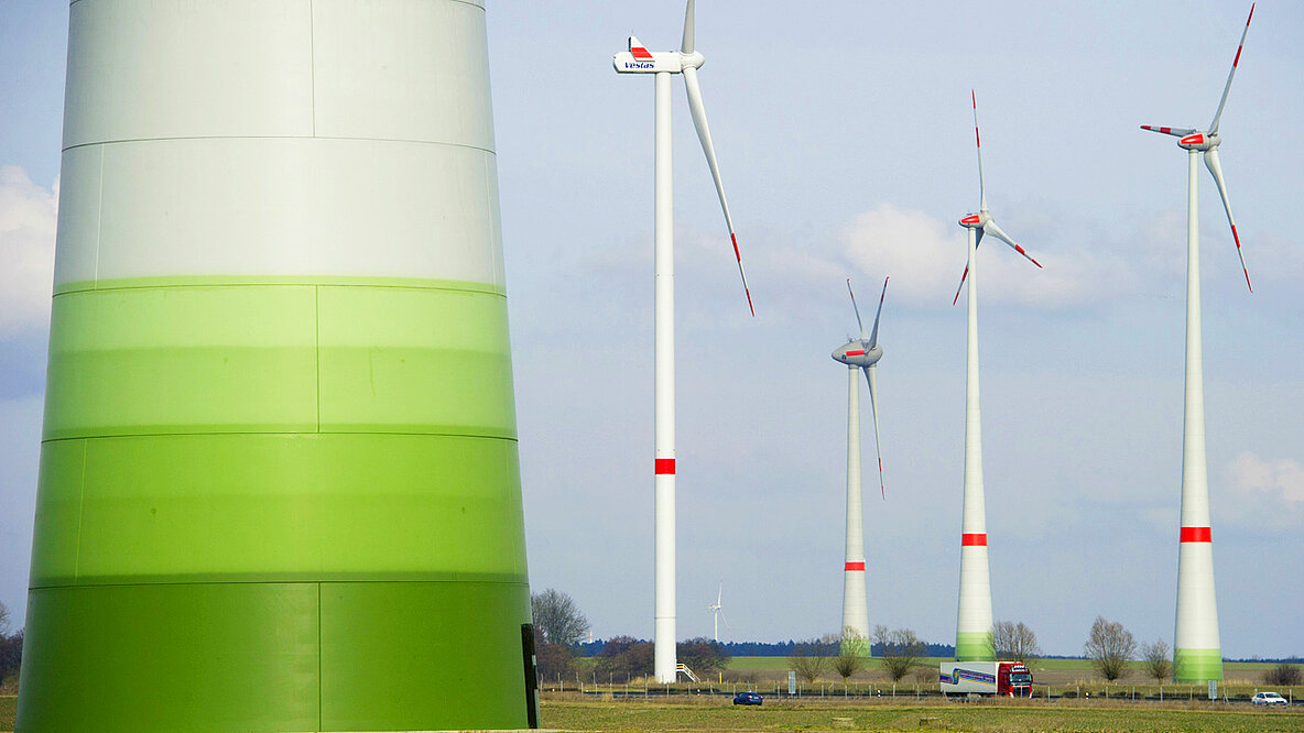 Im Vordergrund der Mast eines Windrades in mehreren Grüntönen, im Hintergrund weitere Windräder.