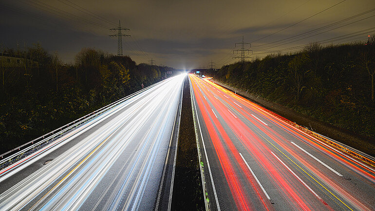 Eine Autobahn bei Nacht. In der Langzeitbelichtung sieht man die verwischten Lichter der Autos.