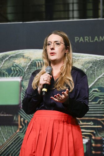 Eine Frau mit wallendem Rock und blonden Haaren spricht auf der Bühne