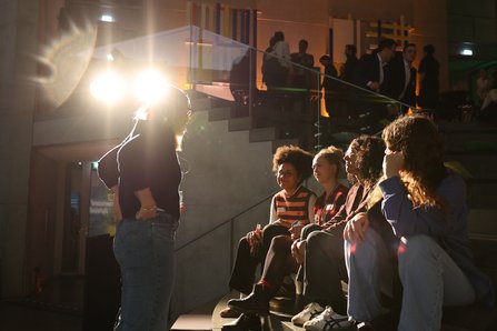mehrere Personen im Gespräch, einige sitzen auf Treppenstufeb