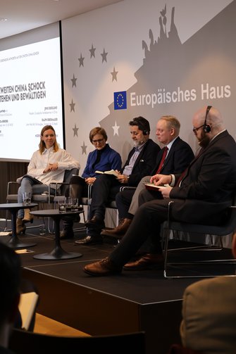 2 Frauen und 3 Männer sitzen auf der Bühne, 2 der Herren tragen Headsets.