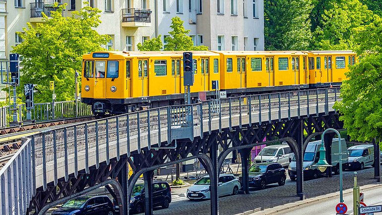 Gelbe U-Bahn fährt auf einer Hochtrasse über Autos auf einer Straße. Ein starker ÖPNV ist die Basis für eine klimafreundliche Mobilität. Ihn auszubauen und zu modernisieren, ist ein zentrales Ziel der Ampel-Koalition.