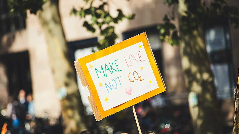 Plakat mit der Aufschrift "Make love not CO2" wird hochgehalten