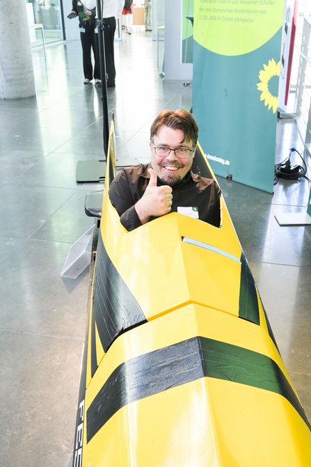 Gelber Doppel-Bob, von vorne, mit lächeldem Mann drin sitzend