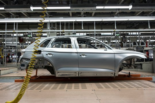 Die unlackierte Rohkarosse eines SUV steht auf einem Montageträger in der Fertigungshalle eines Autowerks.