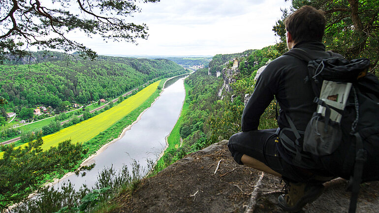 Ein Wanderer sitzt auf einem Felsen in der Nationalparkregion Sächsische Schweiz und schaut ins Elbtal hinab.