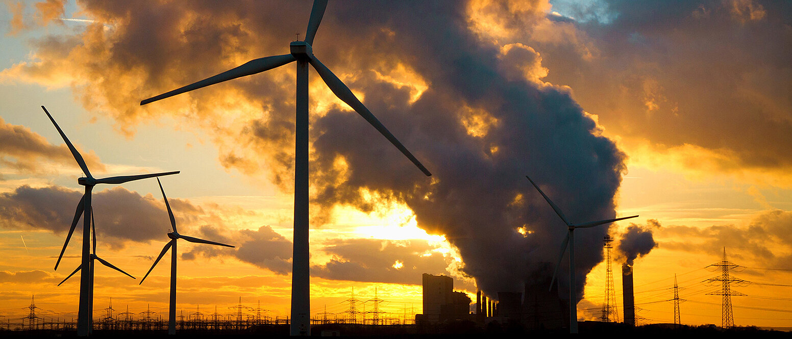 Sonnenuntergang hinter einem großen Kohlekraftwerk und vielen Windkraftanlagen