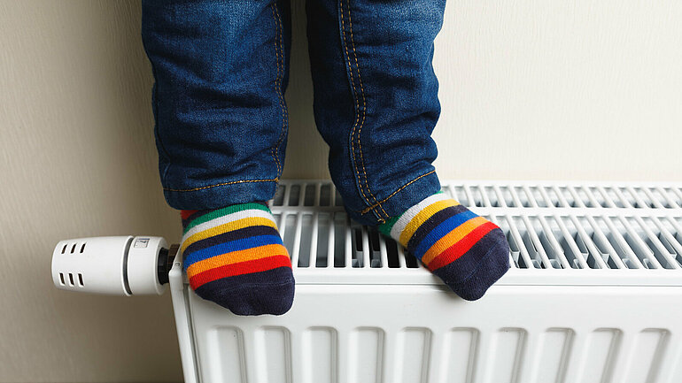 Kinderfüße in farbigen Socken auf einem Heizkörper.
