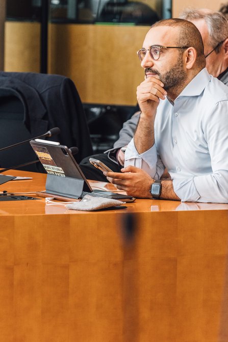 Kassem Taher Saleh hört dem Podiumsgespräch zu, vor ihm befindet sich ein aufgeklappter Tablet-Computer