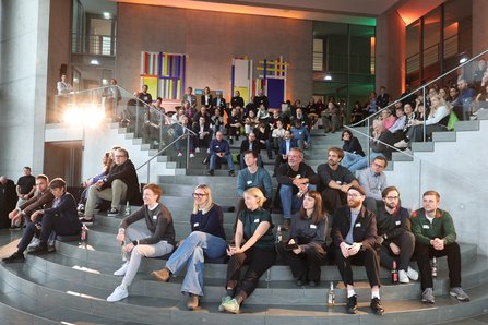 Personen sitzen auf Treppenstufen in einer Art Atrium
