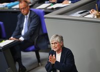 Britta Haßelmann hält am Rednerpult im Plenarsaal eine Rede und Bundeskanzler Friedrich Merz sitzt auf der Regierungsbank.