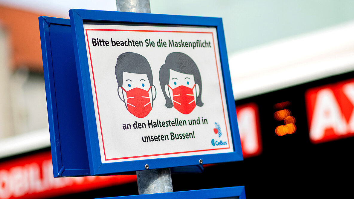 Ein Schild mit der Aufschrift "Bitte beachten Sie die Maskenpflicht an den Haltestellen und in unseren Bussen!" hängt an einer Bushaltestelle im Stadtzentrum. 