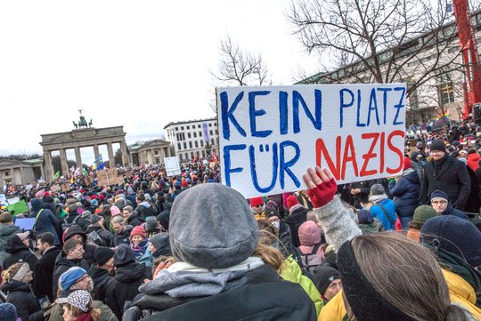 Tausende Menschen demonstrieren am Brandenburger gegen Rechts. Eine Person hält im Vordergrund ein Schild hoch auf dem steht Kein Platz für nazis