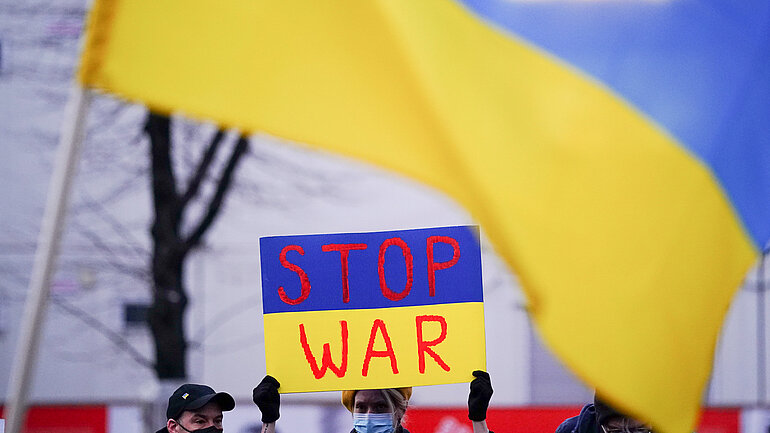 Eine Demonstrantin hält ein Schild mit der Aufschrift "Stop War" in die Kamera.