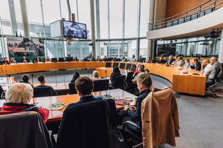 Ein Blick in einen Teil des Europasaals, mit Gästen und Podium, zu sehen sind etwa 40 Personen