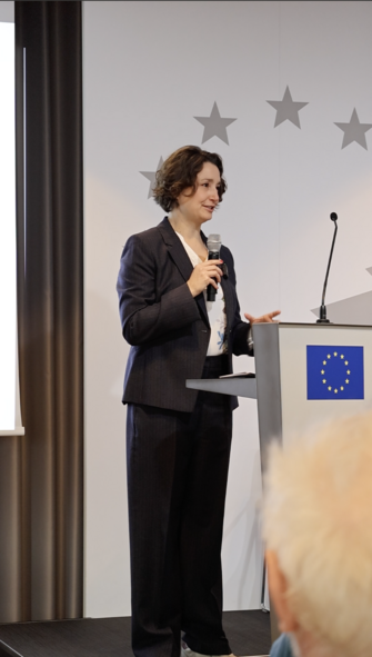 Eine Frau am Redepult, im Hintergrund einige Sterne der europäischen Flagge.