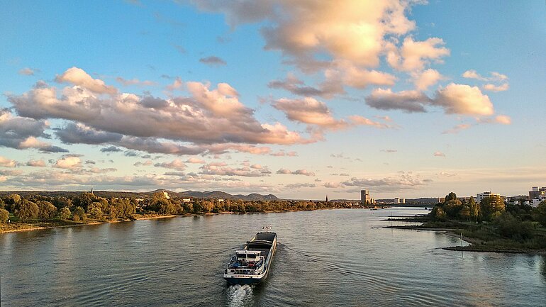 Ein Schiff fährt auf dem Rhein, darüber blauer Himmel und einige Wolken.