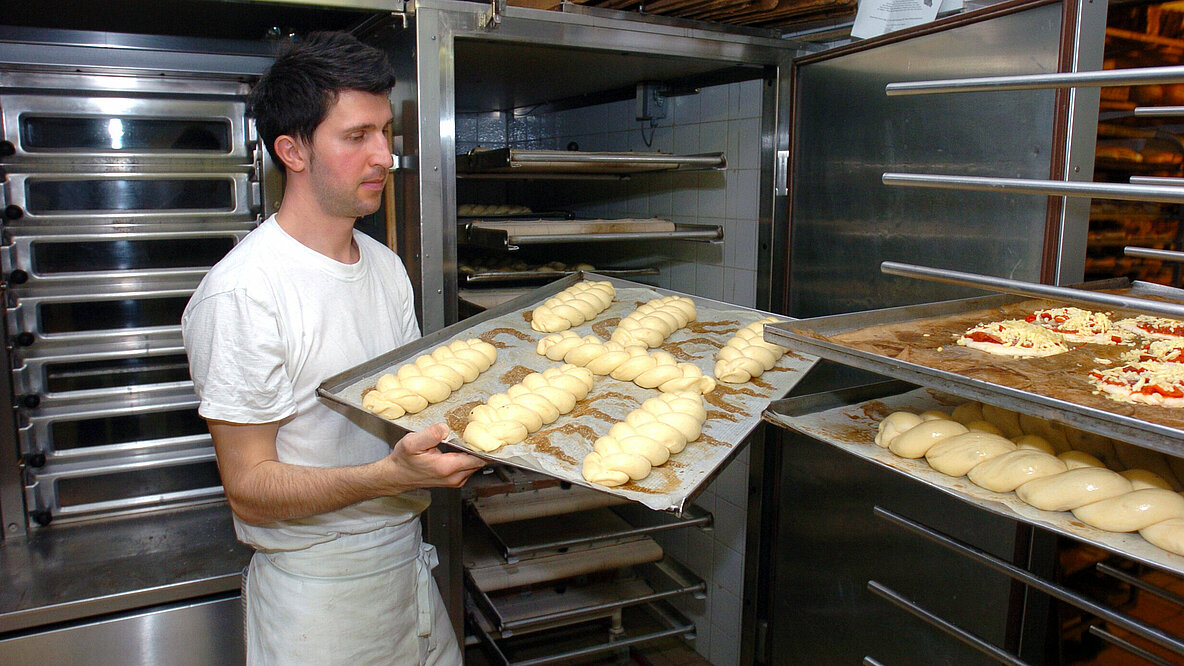 Ein Bäcker hält ein Blech mit Backwaren in den Händen