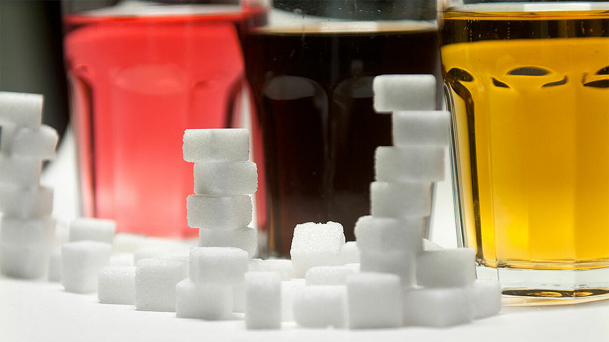 Zuckerhaltige Erfrischungsgetränke und Zuckerwürfel, die den Zuckeranteil symbolisieren