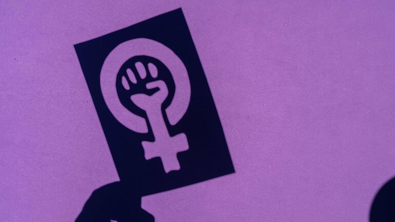 Schatten des Symbols des Kampfes für den Feminismus auf einem lila Hintergrund, geballte Faust einer Frau im Marsch Proteste für die Rechte der Frauen