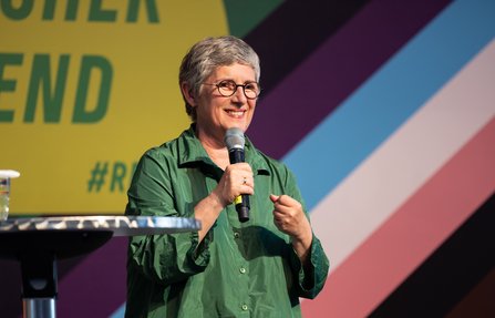 Frau in grünem Kleid auf der Bühne mit Hintergrund Schriftzug Regenbogenabend